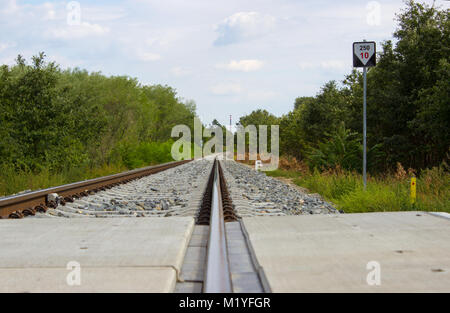 Des voies de chemin de fer sont en retard sur l'horizon. Arbres et buissons sur les côtés. Il y a deux touristes le long de la manière. Banque D'Images