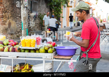 Cartagena, Colombie - Janvier 23th, 2018 : Un vendeur de rue de fruits mangue coupe debout sur la rue avec son panier en bois avec des fruits à Carthagène. Banque D'Images