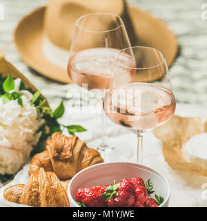 Romantique de style français pique-nique estival. Télévision à jeter des verres de vin rose avec de la glace, de fraises fraîches, croissants, fromage brie, chapeau de paille, la pivoine Banque D'Images