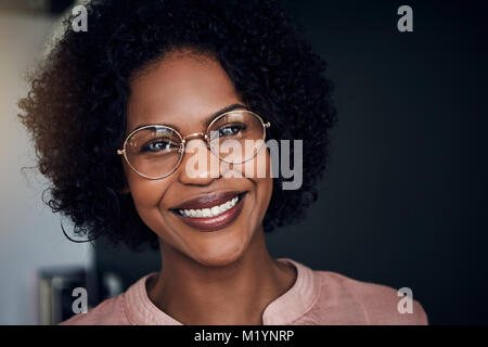 Young African businesswoman wearing glasses avec confiance tout en souriant tout seul dans un bureau moderne Banque D'Images