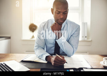 Concentré de jeunes Africains de la lecture des documents et de travailler sur un ordinateur portable tout en étant assis à son bureau dans un bureau Banque D'Images