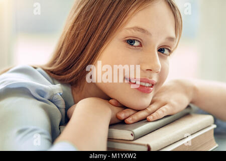 Close up of charming girl resting chin on books Banque D'Images