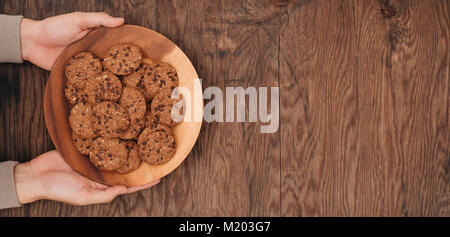 Les cookies au chocolat maison sur plaque dans les mains d'hommes sur table en bois. Banque D'Images