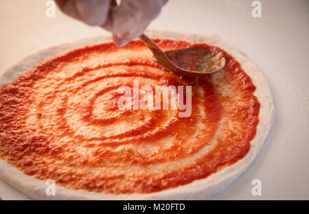 Placer la sauce tomate sur la pâte à pizza Banque D'Images