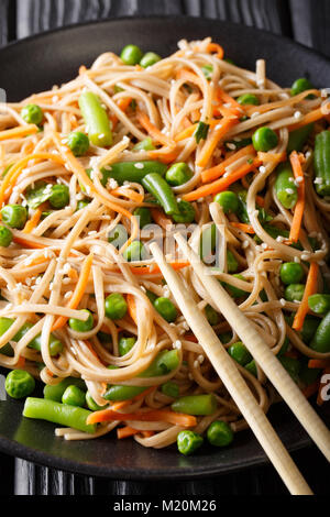 Nouilles de sarrasin avec des carottes, petits pois et haricots verts gros plan sur une plaque verticale, de style japonais. Banque D'Images