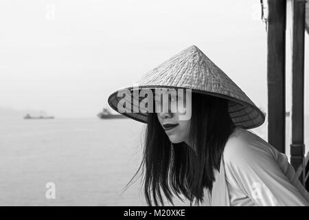 Un jeune Vietnamien woman posing à bord d'un navire dans la baie d'Halong, Vietnam. Elle porte un La, un chapeau conique traditionnel Banque D'Images