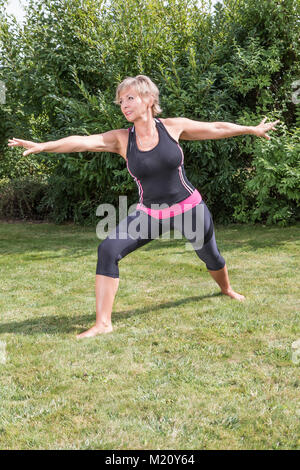 Athletic senior femme blonde l'exercice dans le jardin. Senior woman doing her s'étend à l'extérieur. Banque D'Images