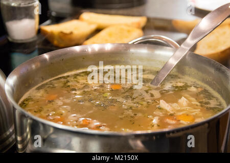 Soupe poulet et nouilles faites maison avec des légumes dans une grande casserole en acier inoxydable avec des tranches de pain grillé à l'arrière-plan Banque D'Images