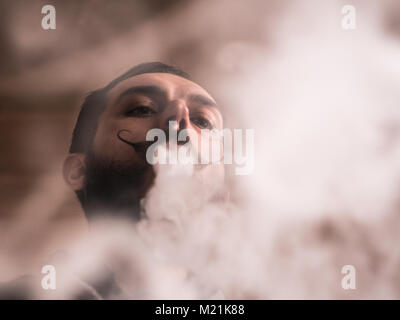 Homme avec Barbe et Mustages Vaping une cigarette électronique. Vaper fumée Hipster vaporisateur et Exhals fumée serré. Banque D'Images