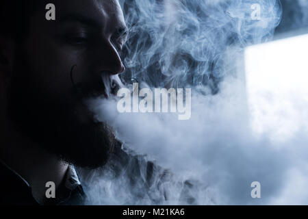 Homme avec Barbe et Mustages Vaping une cigarette électronique. Vaper fumée Hipster vaporisateur et Exhals le débit de fumée. Banque D'Images