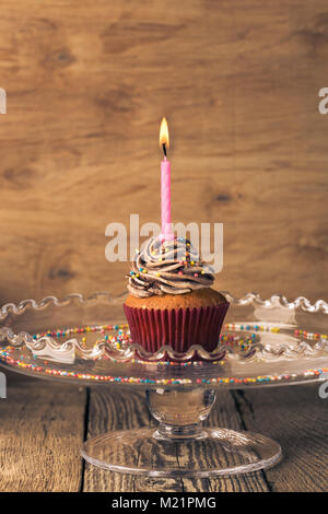 Delicious birthday cupcake avec une bougie servi sur verre cakestand festive sur table en bois, tons rétro Banque D'Images