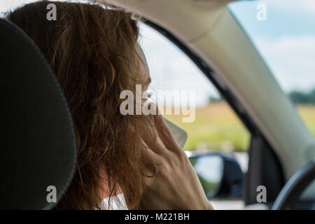 Une jeune femme conduit sa voiture et parle au téléphone et est distrait Banque D'Images