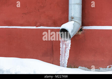 L'eau gelée dans une gouttière pendant la saison d'hiver contre mur rouge grunge background Banque D'Images