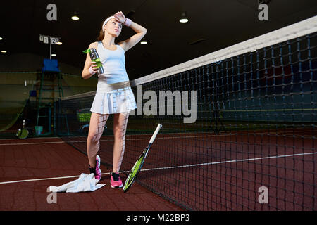 Portrait de l'épuisé tennis player prendre pause dans la pratique l'article contre net et l'eau potable dans la cour intérieure, copy space Banque D'Images