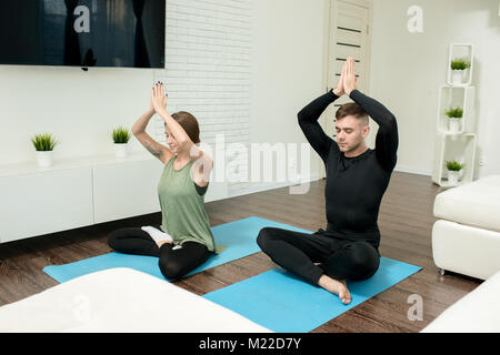 Portrait du jeune couple moderne faisant les exercices de yoga dans la salle de séjour à la maison, méditant en position du lotus, les yeux fermés Banque D'Images