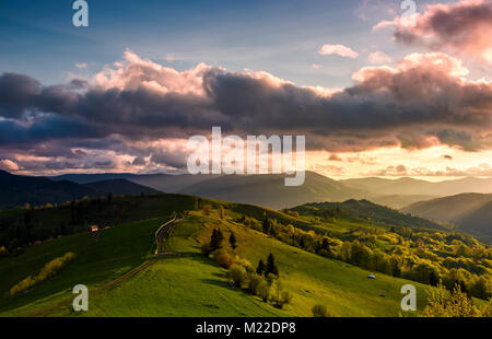 Nuageux glorieux coucher de soleil sur la campagne. beau paysage de printemps avec crête de montagne au loin. chemin serpente à travers des pentes herbeuses o Banque D'Images