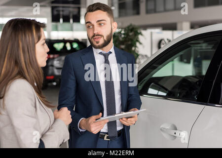 Portrait of handsome car salesman talking to young woman in car showroom aider choisir Banque D'Images