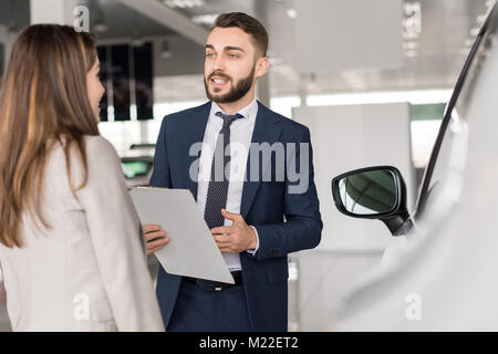 Portrait of handsome car salesman talking to young woman helping her choisissez dans car showroom Banque D'Images