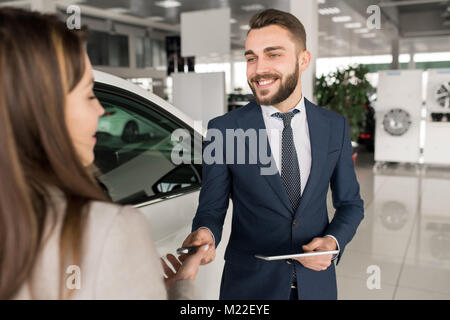 Portrait de beau vendeur de voiture de donner les clés de jeune femme debout à côté de la voiture de luxe brillant blanc dans electronics store Banque D'Images