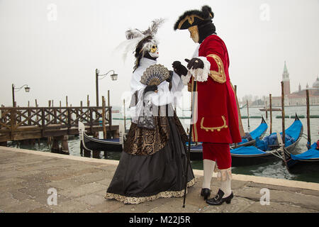 Carnaval de Venise - Couple amoureux des masques vénitiens sur la Place Saint Marc à Venise gondoles avec en arrière-plan. Banque D'Images