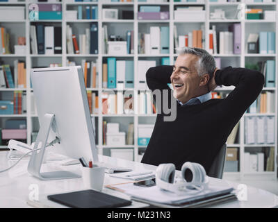 Confiant smiling businessman relaxing dans son bureau avec les mains derrière la tête : la réussite de l'entreprise et concept de réalisation Banque D'Images