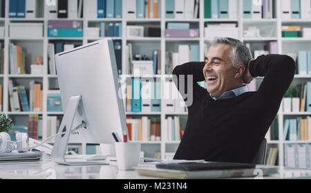 Confiant smiling businessman relaxing dans son bureau avec les mains derrière la tête : la réussite de l'entreprise et concept de réalisation Banque D'Images