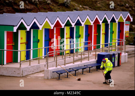 Nettoyant de sable qui a été soufflé sur la digue pendant un vent fort à la cabane de plage salon à Whitmore Bay, Barry Island, Barry, au Pays de Galles Banque D'Images