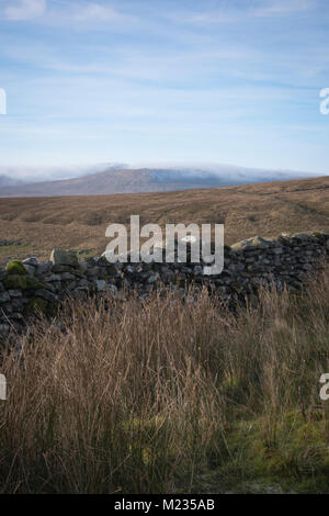 À plus d'un mur de pierres sèches sur le Pennine Way route vers un nuage couverts Ingleborough. Banque D'Images