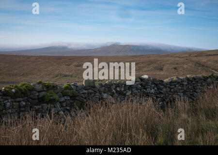 À plus d'un mur de pierres sèches sur le Pennine Way route vers un nuage couverts Ingleborough. Banque D'Images
