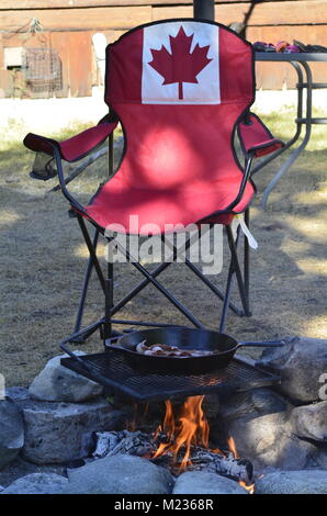 La cuisson du bacon dans une poêle en fonte, sur une grille de cuisson, plus un bain de camp avec un drapeau du Canada président de camp Banque D'Images