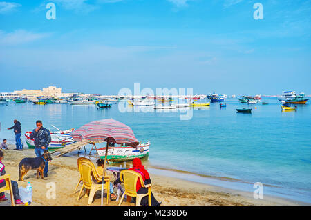 Alexandrie, Egypte - le 17 décembre 2017 : Les gens se détendre sur la côte de sable de l'Est de port avec une vue sur la vieille citadelle de Qaitbay et bateaux de pêche, sur Dece Banque D'Images