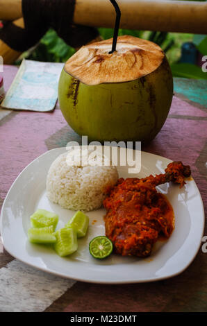 Indonésie : Le plat typique d'Ayam Nasi Plecing (Poulet avec riz et sauce spéciale) et les jeunes noix de coco à la verticale. Banque D'Images