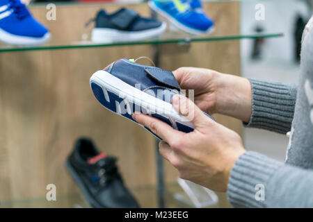 Une femme dans un magasin de chaussures sneakers choisit pour son fils Banque D'Images