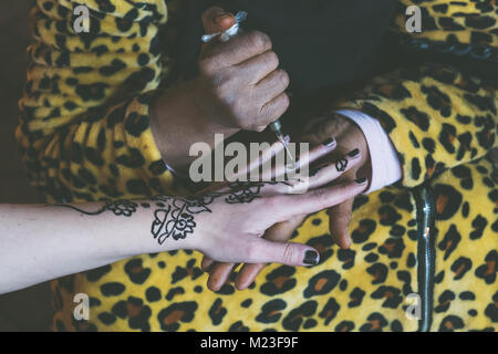 Femme musulmane est en train de faire un tatouage au henné temporaire sur une main de fille blanche Banque D'Images