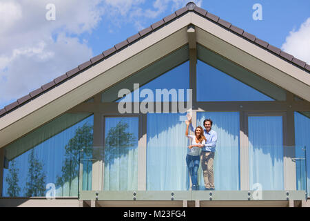 Heureux couple debout sur le balcon de leur chambre et des signes avec la main Banque D'Images