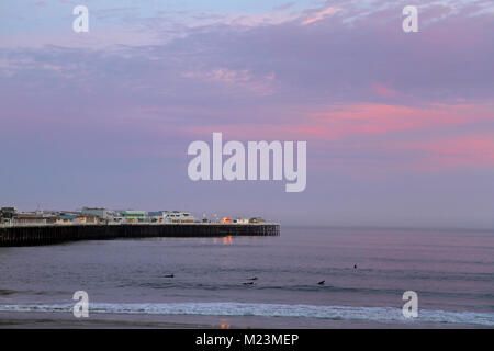 Surfers au coucher du soleil sur la plage de Cowell, quai de Santa Cruz dans l'arrière-plan, Santa Cruz, California, United States Banque D'Images