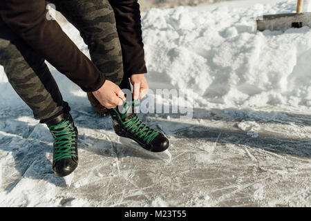 Portrait d'un homme attachant un lacet vert sur ses patins à glace Banque D'Images