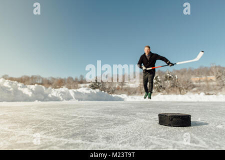 Man playing ice hockey sur un lac gelé en se concentrant sur un puck Banque D'Images