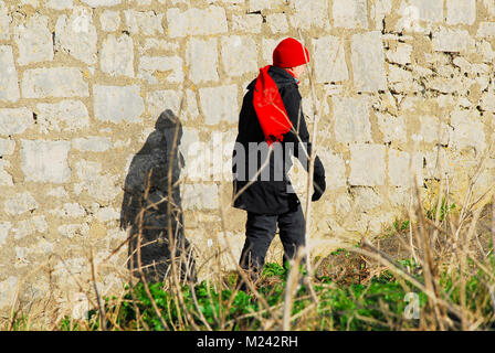 Plage de Chesil, Dorset. 4 février 2018 - une femme plus âgée en tenue pour le vent froid le long de plage de Chesil jette son ombre contre un mur de pierre de Portland dans le soleil de l'après-midi faible crédit : Stuart fretwell/Alamy Live News Banque D'Images