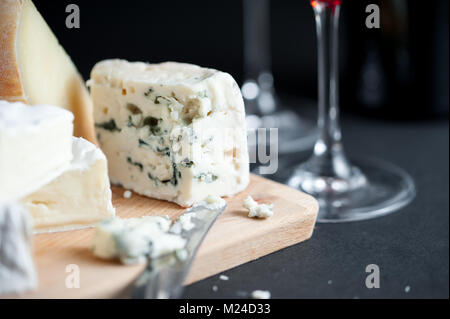 Assiette de fromages avec morceau de Roquefort coupé par couteau vintage et des verres à vin sur un contexte. Fond noir. Image Macro. . Battante Banque D'Images