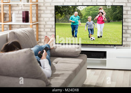 Femme couchée sur le divan à regarder la télévision à la maison Banque D'Images