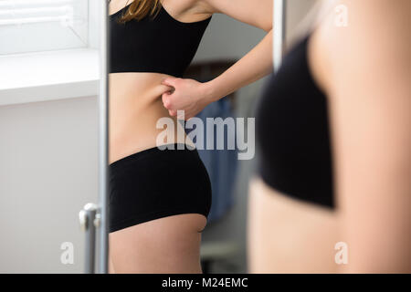La réflexion d'une femme de pincer la peau du ventre dans le miroir Banque D'Images
