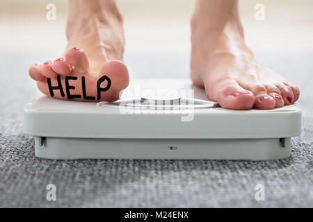 Aider écrit sur le pied d femme debout sur l'échelle de pesage sur le tapis Banque D'Images