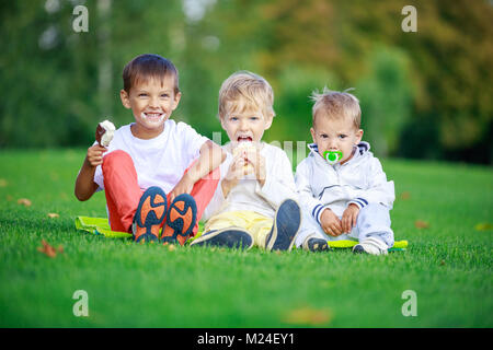 Deux garçons plus âgés la consommation de crème glacée, plus jeune frère de sucer suce alors que sitting on grass in park Banque D'Images