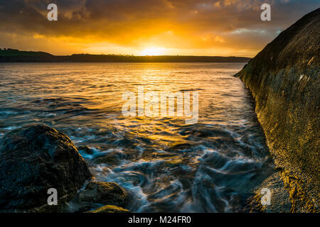 Lever du soleil sur la baie de St Austell à Cornwall avec le béton vieux couverts pipeline et de grosses pierres comme un châssis pour le firey skies au-delà. Banque D'Images