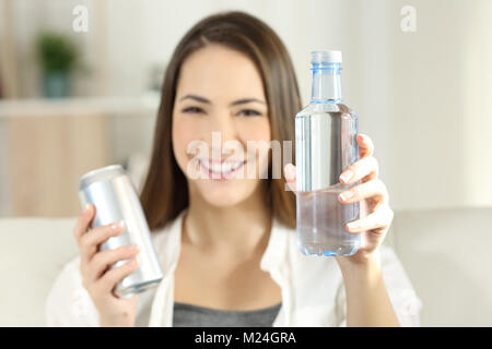 Vue avant portrait d'une femme heureuse montrant une bouteille d'eau et un soda assis sur un canapé dans la salle de séjour à la maison Banque D'Images