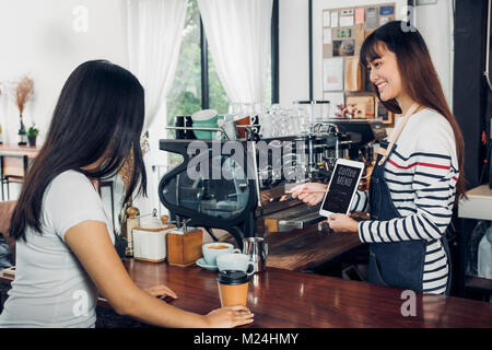 Femme Asiatique jean usure barista café menu suggestion tablier au client au comptoir bar avec smile émotion,Cafe Restaurant service concept propriétaire,petit b Banque D'Images