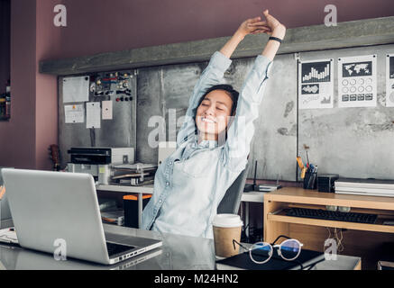 Creative designer asiatique soulever jusqu'à bras et le près en face de l'ordinateur portable sur le bureau,se détendre de dur travail dans bureau. Banque D'Images