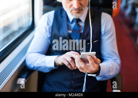 Mature businessman with smartphone voyageant en train. Banque D'Images