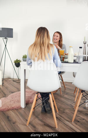 Happy smiling adolescent ayant le petit déjeuner à la maison assis à la table avec une boisson et de la transmission à la personne en face qui est hors de l'écran Banque D'Images